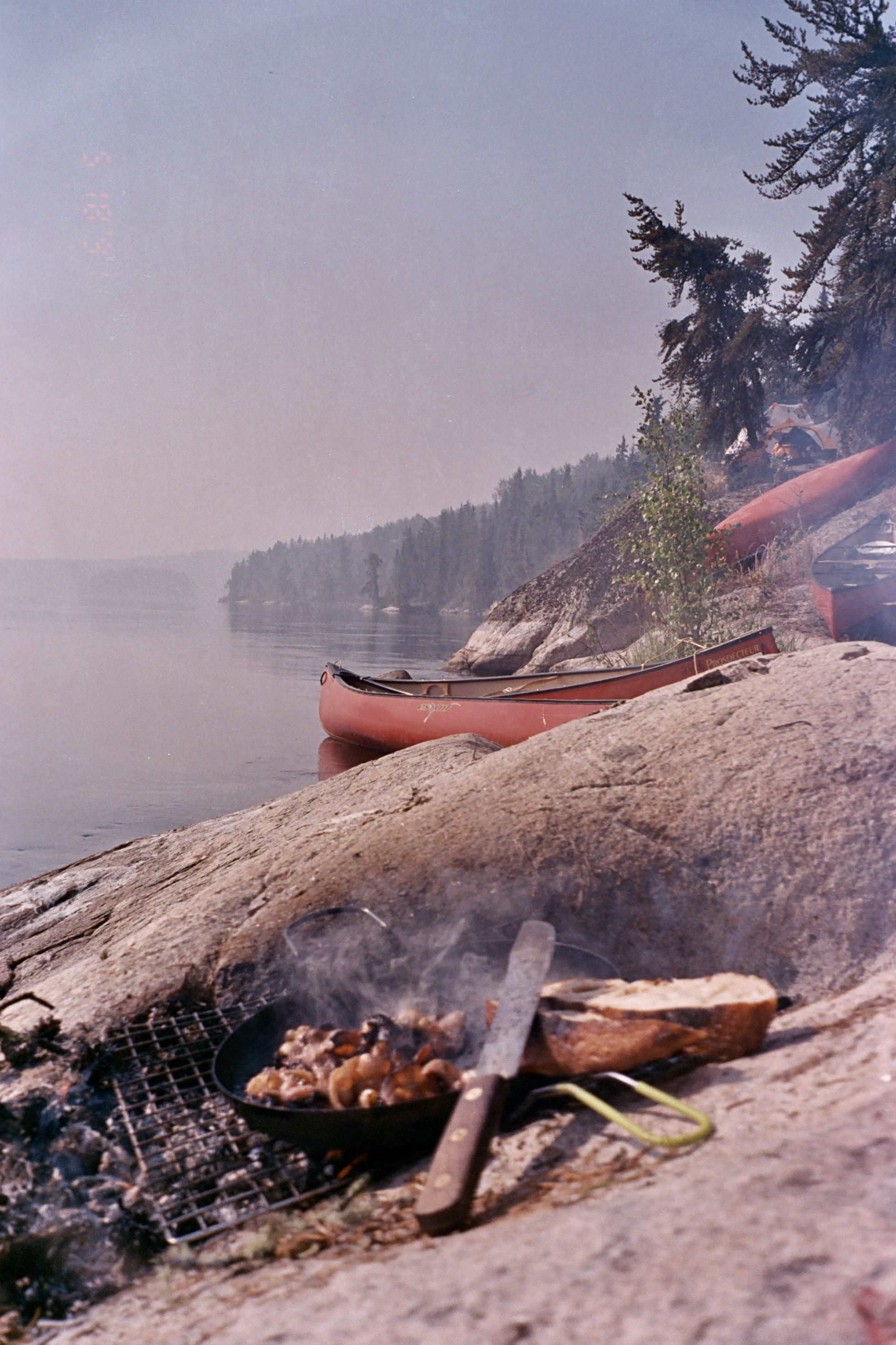 Campfire cooking beside a canoe on a misty lake