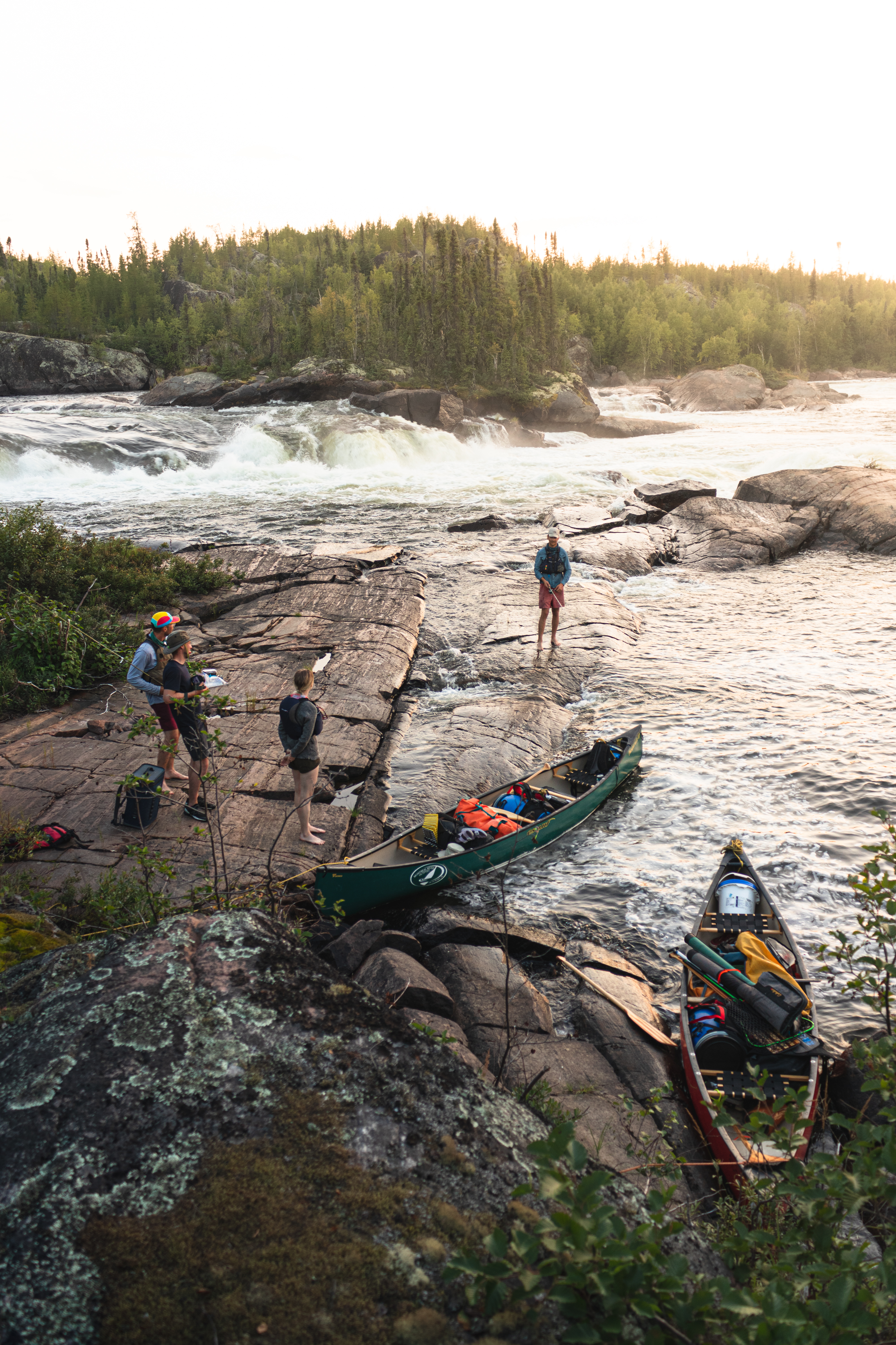 Portaging canoes on a rocky shoreline at golden hour