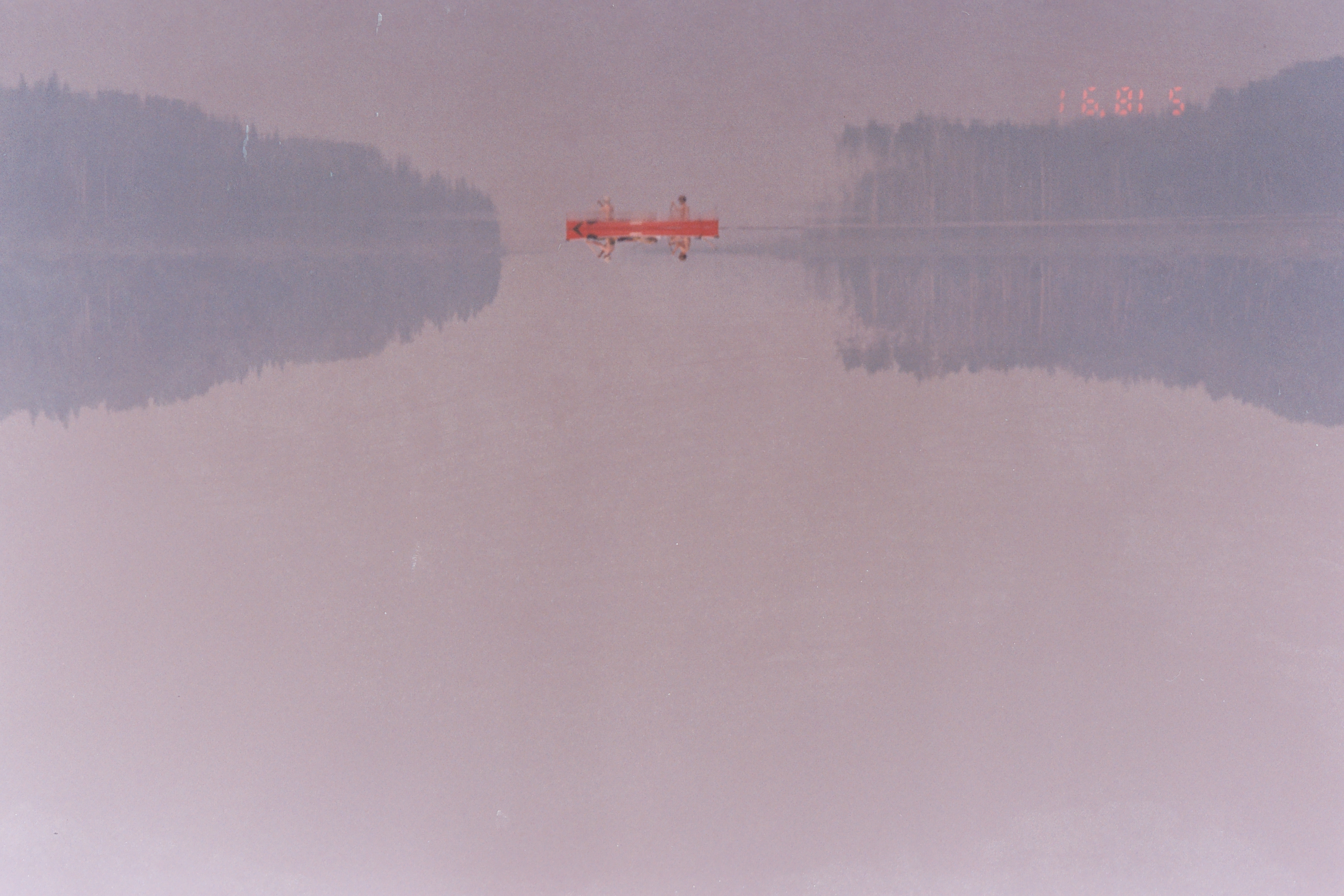 Two people on a red canoe across a glassy, misty lake